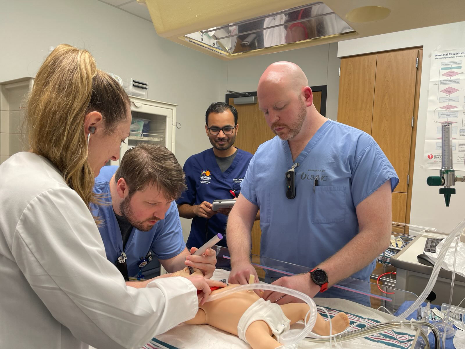 Three medical students simulating an intubation on an infant dummy as a doctor looks on.